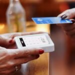 Person making a contactless payment with a credit card, representing the concept of FICO score vs credit score and their differences.