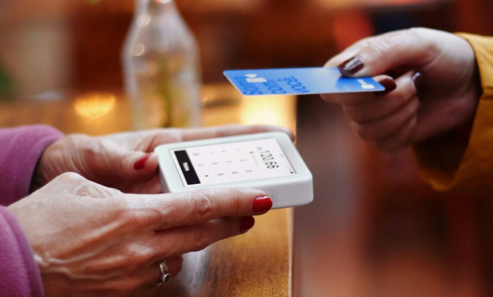 Person making a contactless payment with a credit card, representing the concept of FICO score vs credit score and their differences.