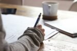 Person writing financial notes on a desk with a coffee cup and notebook, illustrating Personal Finance Advice, personal finance management, personal finance for beginners, and wealth management.