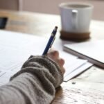Person writing financial notes on a desk with a coffee cup and notebook, illustrating Personal Finance Advice, personal finance management, personal finance for beginners, and wealth management.