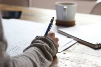 Person writing financial notes on a desk with a coffee cup and notebook, illustrating Personal Finance Advice, personal finance management, personal finance for beginners, and wealth management.